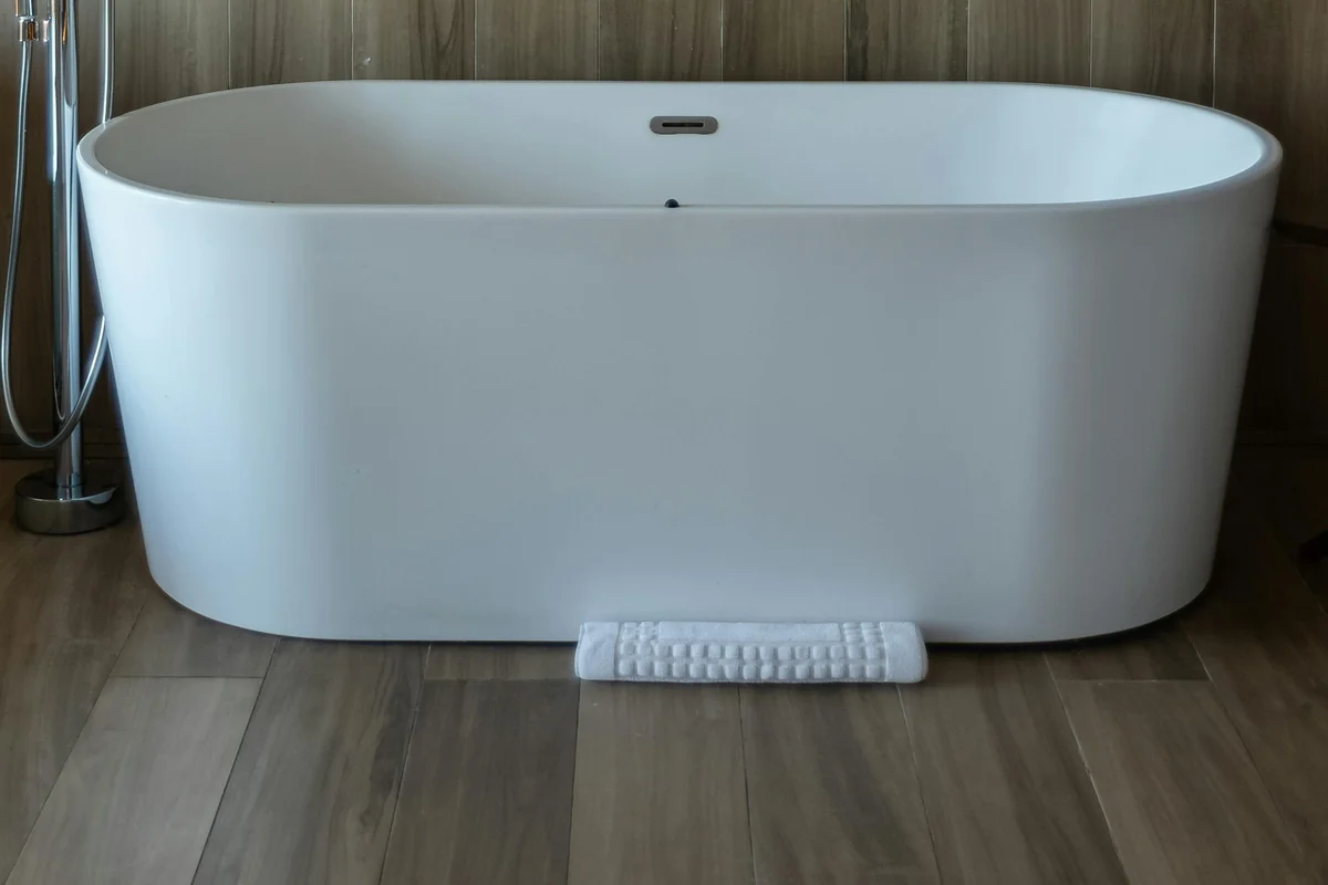 Torneira de coluna de chão junto a banheira freestanding branca, pavimento em madeira