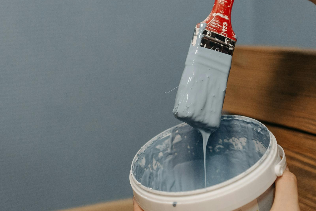 Pincel carregado com tinta exterior a ser mergulhado em balde — preparação para aplicação de tinta em móveis de jardim em madeira