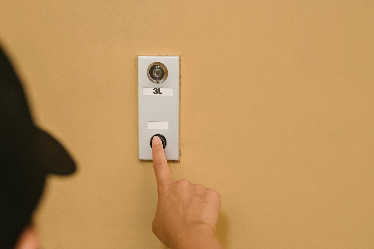 Mão a pressionar botão de campainha na parede