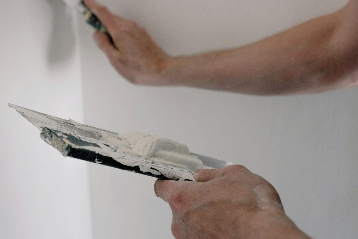 Trabalhador a nivelar e alisar massa de estuque na parede com desempenadeira em movimentos circulares