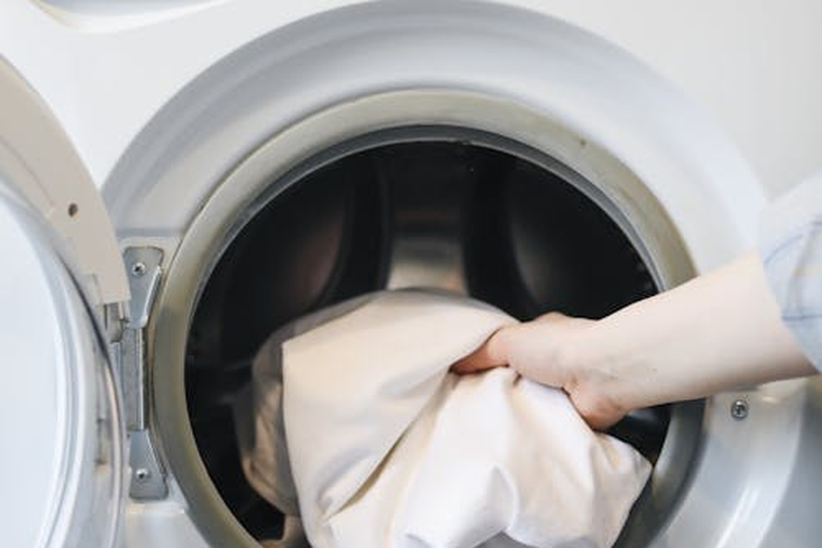 Mão a abrir a porta de uma máquina de lavar roupa de carregamento frontal para inspecionar o vedante
