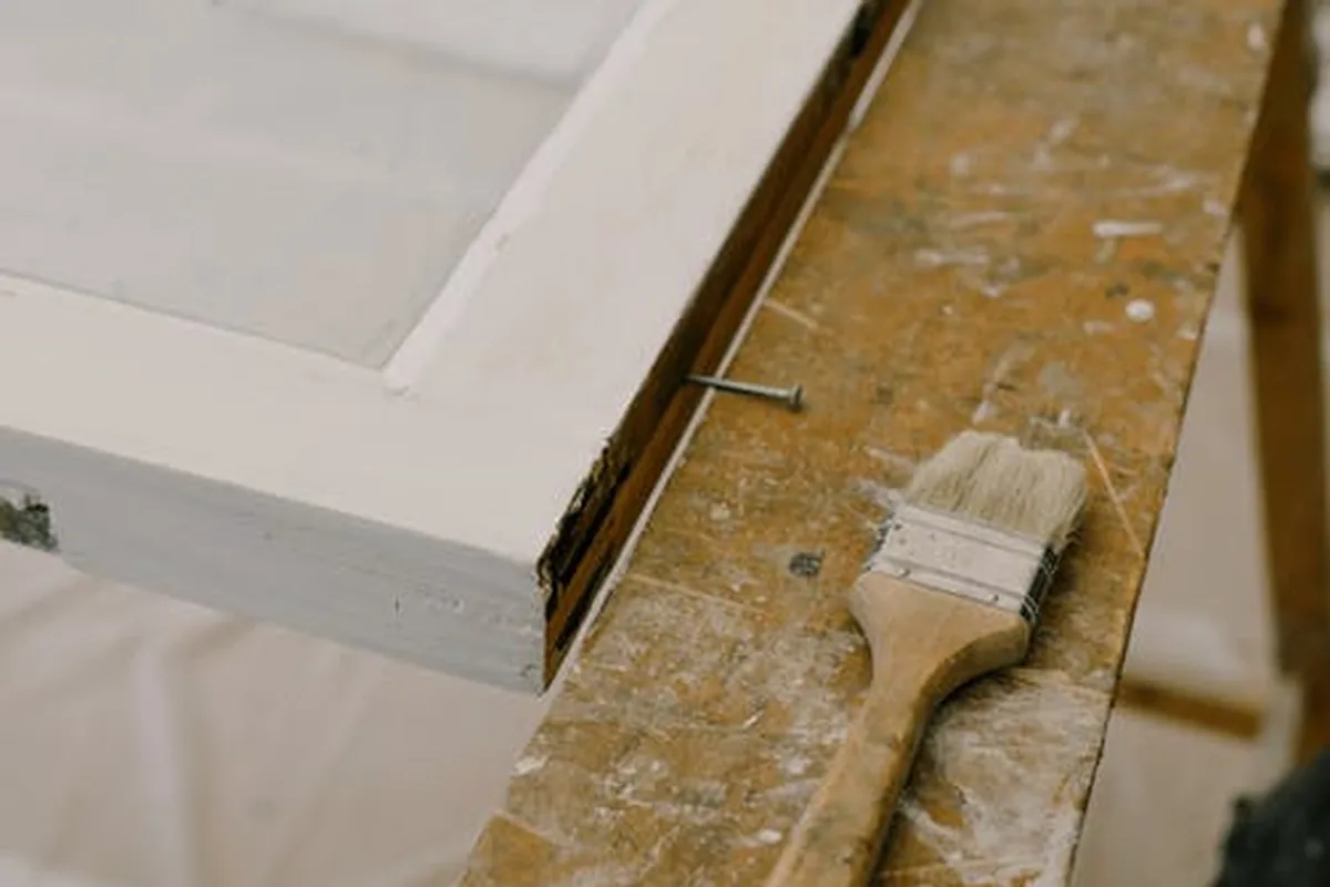 Carpinteiro a pintar caixilho de madeira com pincel, aplicando demão de acabamento exterior